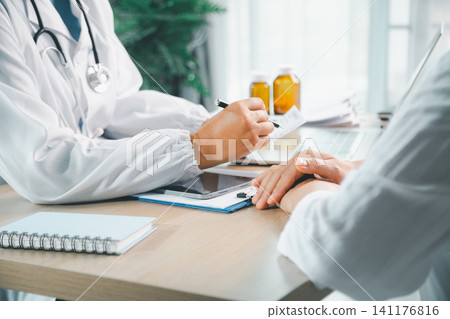 Doctor writing prescription notes while consulting patient in a clinic, healthcare service, medical document, medication advice, treatment plan, and patient care concept. Doctor writing prescription notes while consulting patient in a clinic, healthcare service, medical document, medication advice, treatment plan, and patient care concept. 141176816
