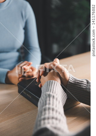 Close up of caring hands holding together over Holy Bible with wooden cross, showing Christian prayer support, pastoral care, compassion and healing. 141176882