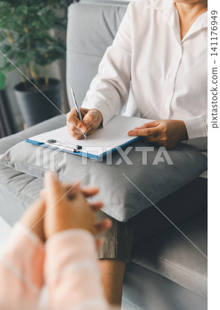 Therapist takes notes on clipboard as female client shares concerns during counseling, showing active listening, mental health support, emotional care, empathy, communication. Therapist takes notes on clipboard as female client shares concerns during counseling, showing active listening, mental health support, emotional care, empathy, communication. 141176949