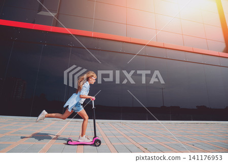 Little girl riding scooter outdoors. Street urban background Little girl riding scooter outdoors. Street urban background 141176953