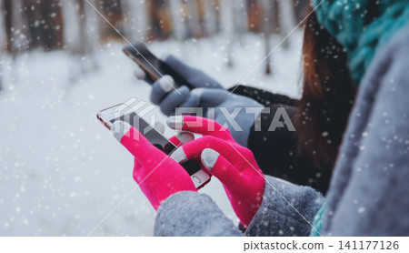 Couple using smartphone in winter with gloves for touch screens Couple using smartphone in winter with gloves for touch screens 141177126