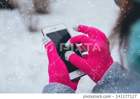 Woman using smartphone in winter with gloves for touch screens Woman using smartphone in winter with gloves for touch screens 141177127