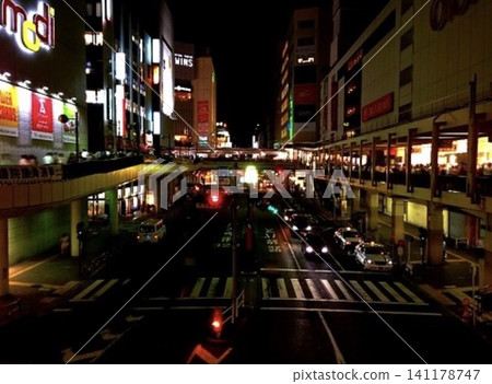 Neon lights and streetlights illuminate the area in front of the station at night. The city lights and the bustling cityscape. Neon lights and streetlights illuminate the area in front of the station at night. The city lights and the bustling cityscape. 141178747
