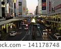 黃昏時分的車站前，夕陽的餘暉灑在天空，城市燈光開始亮起，構成了一幅生氣勃勃的都市景象。 141178748