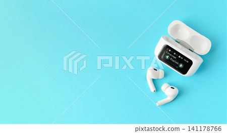 White wireless earbuds with a smart charging case on a blue background. Modern audio technology concept for music, communication and mobile lifestyle White wireless earbuds with a smart charging case on a blue background. Modern audio technology concept for music, communication and mobile lifestyle 141178766