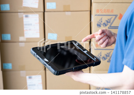 A man's hands using a tablet in a warehouse A man's hands using a tablet in a warehouse 141178857