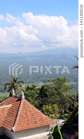 Terracotta roof with palm trees above lush tropical valley, village hillside, distant mountains, blue sky and soft clouds, capturing warm island landscape and traditional charm Terracotta roof with palm trees above lush tropical valley, village hillside, distant mountains, blue sky and soft clouds, capturing warm island landscape and traditional charm 141180016
