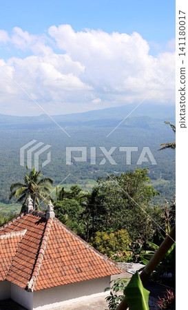Traditional terracotta roof and tropical valley viewed from hillside with palm trees and distant mountains under blue sky with clouds Traditional terracotta roof and tropical valley viewed from hillside with palm trees and distant mountains under blue sky with clouds 141180017