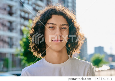 Happy curly haired teenage boy smiling outdoors on modern city street background 141180405