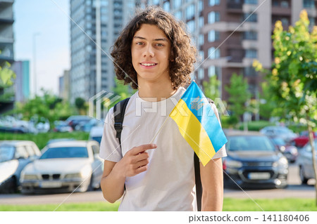 Happy Ukrainian teenage boy with small national flag standing outdoors in city 141180406