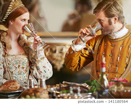 Couple, noble and wine with luxury, feast and renaissance dining table at royal home. King, queen and food with wealth, rich meal and palace or manor for romance with historical chalice and drink Couple, noble and wine with luxury, feast and renaissance dining table at royal home. King, queen and food with wealth, rich meal and palace or manor for romance with historical chalice and drink 141180564
