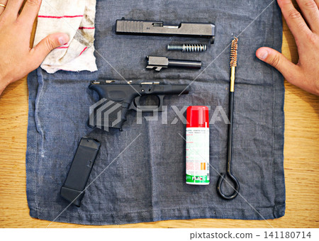Hands, cleaning and man with gun on cloth for safety, self defense and handgun assembly. Process, equipment and person with firearm maintenance, magazine and metal parts to assemble weapon on table Hands, cleaning and man with gun on cloth for safety, self defense and handgun assembly. Process, equipment and person with firearm maintenance, magazine and metal parts to assemble weapon on table 141180714