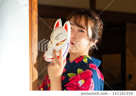 A woman in a yukata wearing a fox mask A woman in a yukata wearing a fox mask 141181359