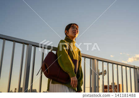 黃昏時分,手提包的女子抬頭眺望城市天際線。 黃昏時分,手提包的女子抬頭眺望城市天際線。 141181488