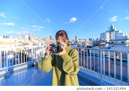 一位女士手持相機，背景是城市景觀。 141181494