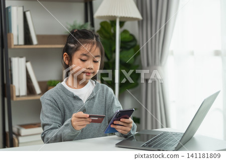 Young Asian girl using smartphone and holding credit card for online shopping at home with laptop on table in comfortable living room setting Young Asian girl using smartphone and holding credit card for online shopping at home with laptop on table in comfortable living room setting 141181809