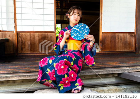 一位女子坐在陽台上,手裡拿著一把扇子。 一位女子坐在陽台上,手裡拿著一把扇子。 141182110