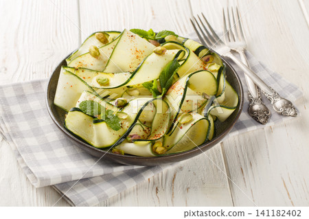 Zucchini Carpaccio is a raw courgettes salad with with pistachios, chili pepper and mint close-up in a plate. Horizontal Zucchini Carpaccio is a raw courgettes salad with with pistachios, chili pepper and mint close-up in a plate. Horizontal 141182402