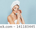 Woman with towel wrapped head applies eye patches 141183445