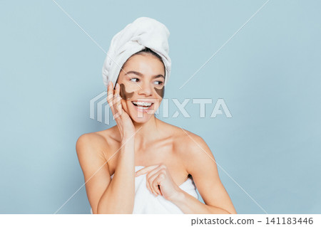 Smiling woman with face mask and towel, light blue background Smiling woman with face mask and towel, light blue background 141183446