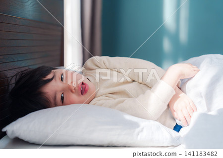 A small child suffering in bed with a fever. A small child suffering in bed with a fever. 141183482