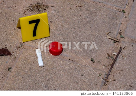 One yellow crime scene marker on the paving slab near a bottle cap and a cigarette butt One yellow crime scene marker on the paving slab near a bottle cap and a cigarette butt 141183866