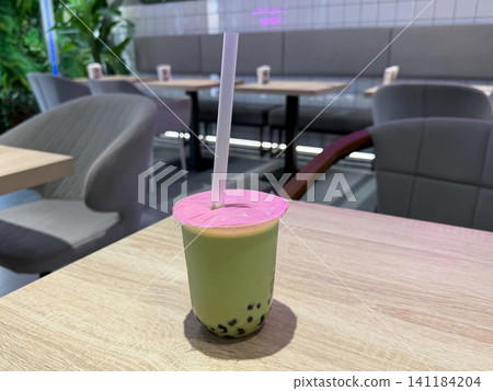 Matcha bubble tea with tapioca pearls served on cafe table in modern interior with soft background blur. Cafe culture, food trend, lifestyle, refreshment, beverage, takeaway, social media Matcha bubble tea with tapioca pearls served on cafe table in modern interior with soft background blur. Cafe culture, food trend, lifestyle, refreshment, beverage, takeaway, social media 141184204