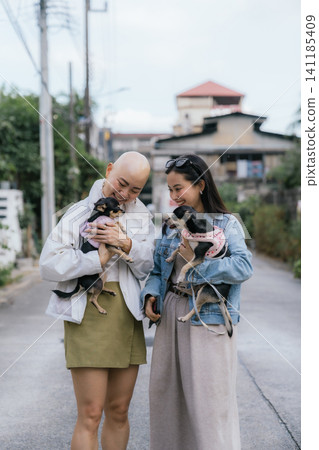 Smiling women friends holding small dogs on street street Smiling women friends holding small dogs on street street 141185409
