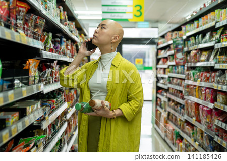 Woman talking on phone while shopping in supermarket aisle Woman talking on phone while shopping in supermarket aisle 141185426