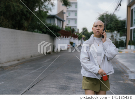 Bald woman walking dog on street talking on smartphone Bald woman walking dog on street talking on smartphone 141185428
