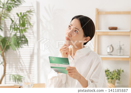 A middle-aged woman looking at her bankbook and worrying A middle-aged woman looking at her bankbook and worrying 141185887