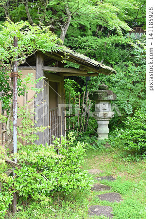 A stone lantern and a simple waiting room stand amidst the fresh greenery; a moss-covered path surrounded by beautiful trees and a wooden hut evoke the traditional beauty and tranquility of the tea ceremony. A stone lantern and a simple waiting room stand amidst the fresh greenery; a moss-covered path surrounded by beautiful trees and a wooden hut evoke the traditional beauty and tranquility of the tea ceremony. 141185928
