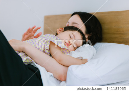 一個女孩和她的母親睡在同一張床上。 一個女孩和她的母親睡在同一張床上。 141185965