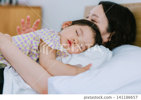 一個女孩和她的母親睡在同一張床上。 一個女孩和她的母親睡在同一張床上。 141186657