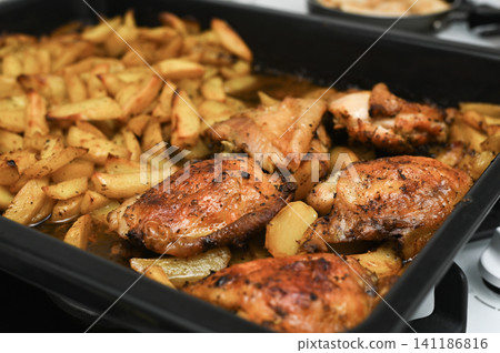Baked chicken pieces served with crispy potato slices on black tray. Baked chicken pieces served with crispy potato slices on black tray. 141186816