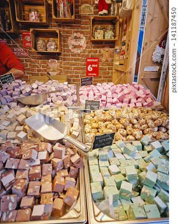 Paris, France - December 10, 2025: Colorful vendor stall displays artisanal nougat cubes in various flavors. Cheerful holiday confectionery atmosphere at the Tuileries Christmas Market Paris, France - December 10, 2025: Colorful vendor stall displays artisanal nougat cubes in various flavors. Cheerful holiday confectionery atmosphere at the Tuileries Christmas Market 141187450