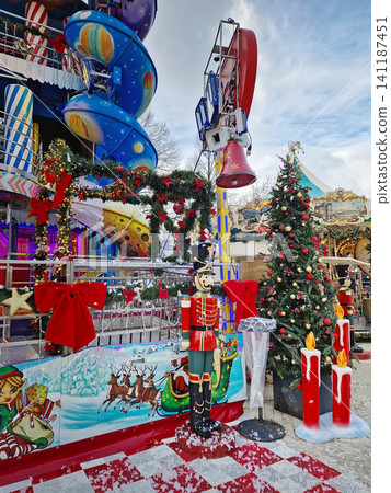 Paris, France - December 10, 2025 Festive outdoor amusement park at the Tuileries Christmas Market, with a Nutcracker soldier stands under simulated snow beside a Christmas tree and a holiday carousel Paris, France - December 10, 2025 Festive outdoor amusement park at the Tuileries Christmas Market, with a Nutcracker soldier stands under simulated snow beside a Christmas tree and a holiday carousel 141187451