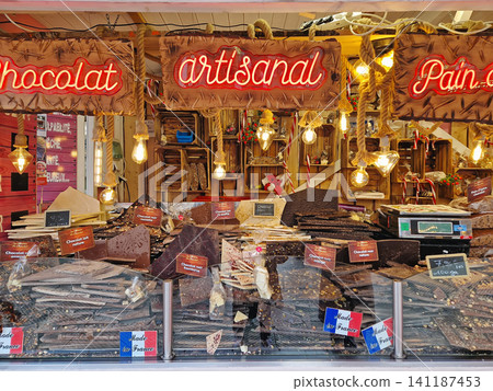 Paris, France - December 10, 2025: rustic vendor stall showcases large slabs of artisanal French chocolate in dark, milk, and white varieties. Festive holiday display at the Tuileries Christmas Market Paris, France - December 10, 2025: rustic vendor stall showcases large slabs of artisanal French chocolate in dark, milk, and white varieties. Festive holiday display at the Tuileries Christmas Market 141187453
