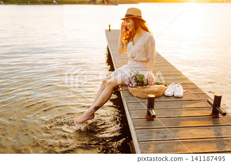 Young woman in dress sitting on wooden pier near pond. Rustic style of wedding. Travel, tourism Young woman in dress sitting on wooden pier near pond. Rustic style of wedding. Travel, tourism 141187495