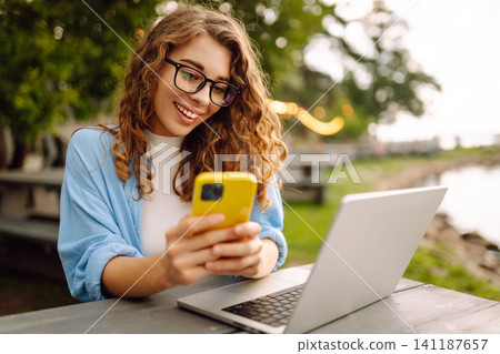Freelancer woman with phone enjoying the weather on lake. Technology, freelancing or leisure concept Freelancer woman with phone enjoying the weather on lake. Technology, freelancing or leisure concept 141187657