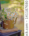 Brass retro teapot with daisies and an old book on a chair 141187680