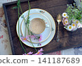 Coffee with milk in a porcelain cup, a milk jug and wildflowers on a wooden tray 141187689