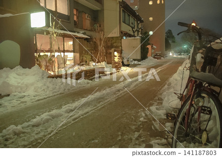 A bicycle stands on Saisei Road at night, where snow still remains, and a building from which warm light spills out. A bicycle stands on Saisei Road at night, where snow still remains, and a building from which warm light spills out. 141187803