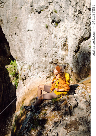 Smiling female dressed in hiking clothes, enjoys a waterfall near a mountain river. Travel, trekking Smiling female dressed in hiking clothes, enjoys a waterfall near a mountain river. Travel, trekking 141187883