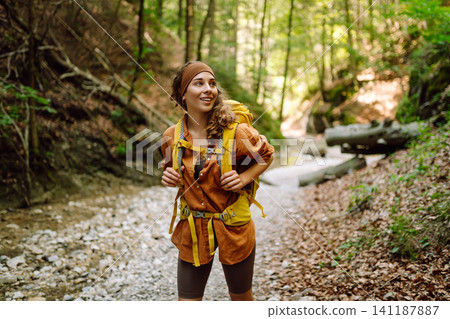 A traveler walks along forest hiking trail in mountains on a sunny day. Outdoor recreation concept. A traveler walks along forest hiking trail in mountains on a sunny day. Outdoor recreation concept. 141187887