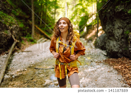 A traveler walks along forest hiking trail in mountains on a sunny day. Outdoor recreation concept. A traveler walks along forest hiking trail in mountains on a sunny day. Outdoor recreation concept. 141187889