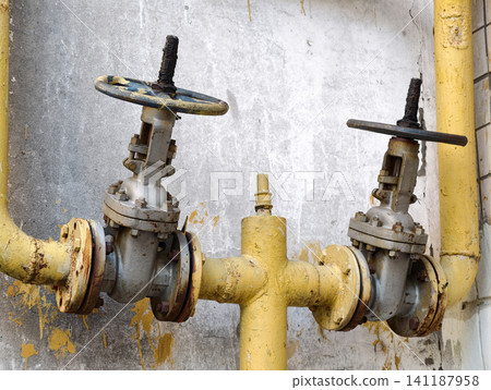 Gas shut off mechanisms positioned on residential building exterior with yellow painted pipelines and industrial engineering structure 141187958