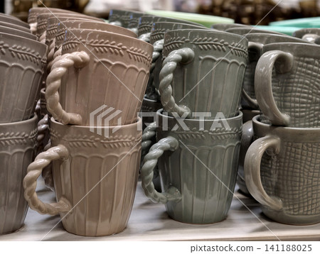 Ceramic cups in deep dark shades with twisted handles arranged on store shelves showing basic tableware assortment intended for daily kitchen use and practical retail presentation Ceramic cups in deep dark shades with twisted handles arranged on store shelves showing basic tableware assortment intended for daily kitchen use and practical retail presentation 141188025