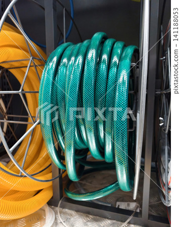 Green hose rolled into a compact coil is presented in a retail hardware store for general water and utility use 141188053