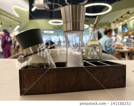 Tabletop arrangement with salt, pepper, oil in clear glass bottles and napkins displayed in close up, representing common restaurant dining essentials 141188252